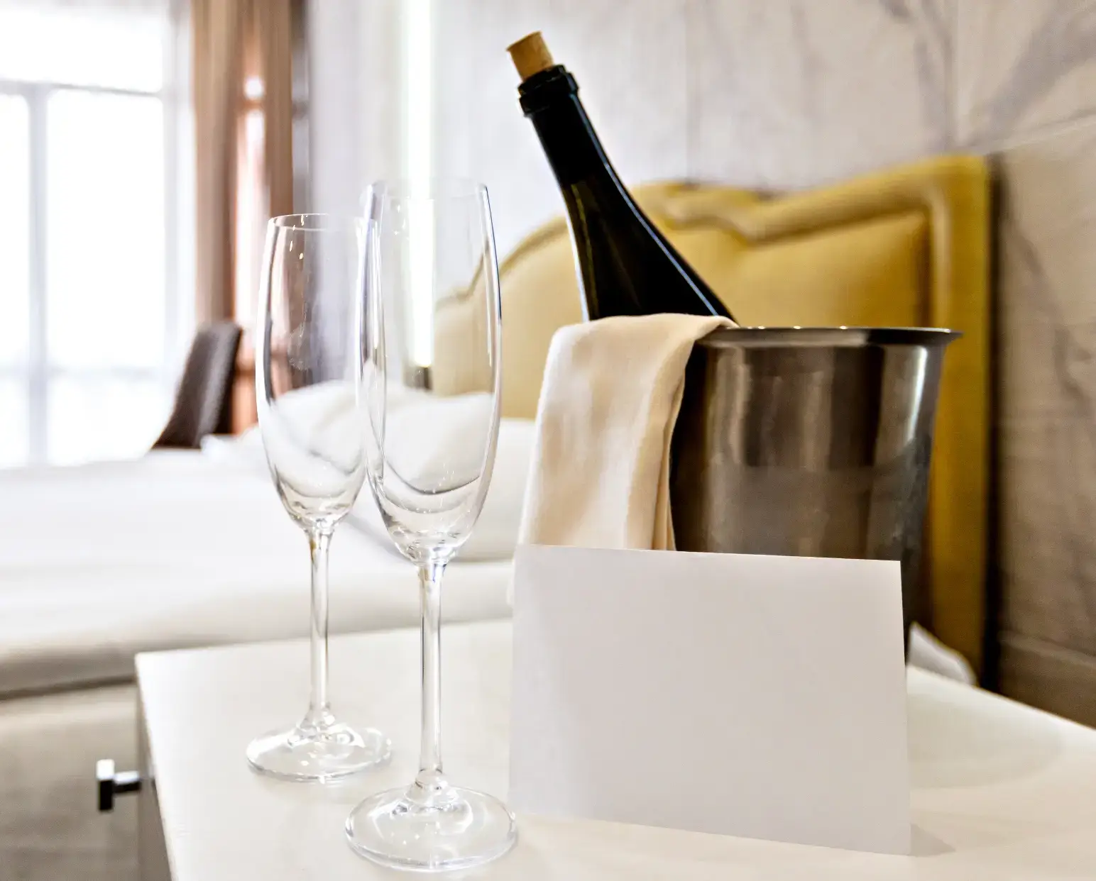 Bottle of champagne in an ice bucket with champagne flutes on the side next to a hotel room bed in Point Pleasant Beach, NJ